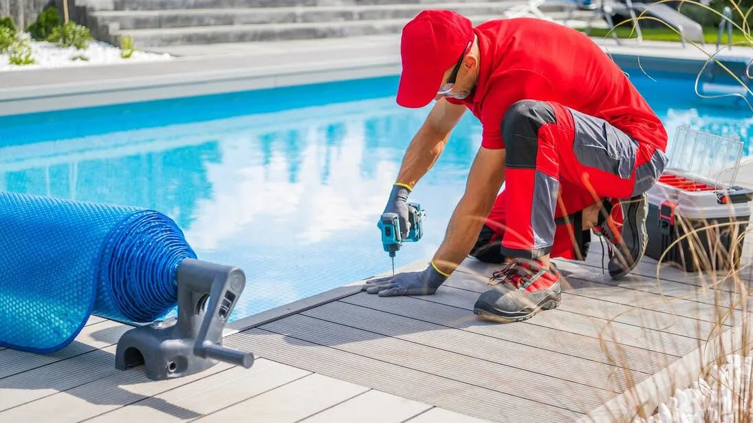 Person in red shirt and gray pants working by a poolside with blue pool cover and tools.