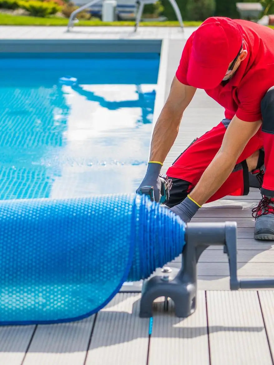Person in red hoodie and gloves working on a pool cover by a swimming pool.